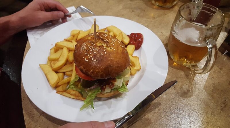 Hambúrguer acompanhado de batatas fritas e bebida em restaurante. Imagem ilustrativa.